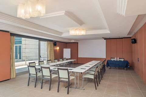 Meeting room setup with U-shaped tables, chairs, a projector screen, and a table covered with a blue cloth at B&B Hotel San Mauro