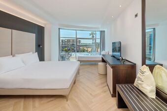 B&B Hotel San Mauro modern guest room with two beds, large window with urban view, TV, wardrobe, and light wood flooring