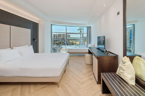 B&B Hotel San Mauro modern guest room with two beds, large window with urban view, TV, wardrobe, and light wood flooring