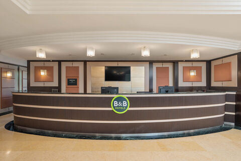 Reception desk with computers, a large wall-mounted TV, and decorative panels at B&B Hotel San Mauro