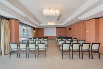Conference room at B&B Hotel San Mauro with rows of chairs facing a projector screen and peach-colored walls