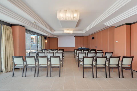 Conference room at B&B Hotel San Mauro with rows of chairs facing a projector screen and peach-colored walls