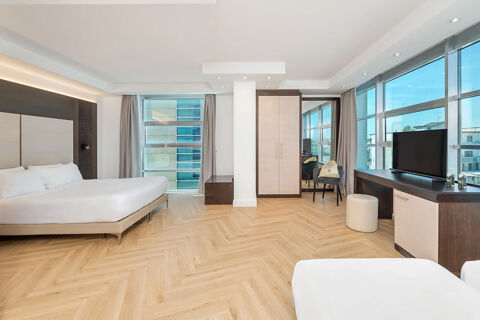 Spacious hotel room at B&B Hotel San Mauro with two beds, large windows, wooden floors, a wardrobe, and a TV on a desk