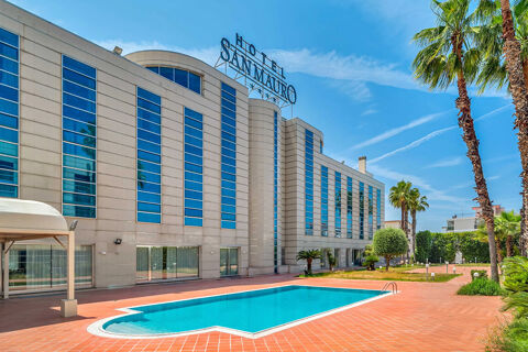 Modern building of B&B Hotel San Mauro with multiple windows, a swimming pool, palm trees, and a clear blue sky