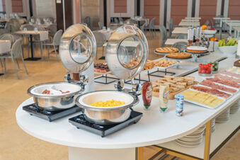 Breakfast buffet at B&B Hotel San Mauro featuring scrambled eggs, bread, cold cuts, cheese, pastries, fruit, and sauces on a white table