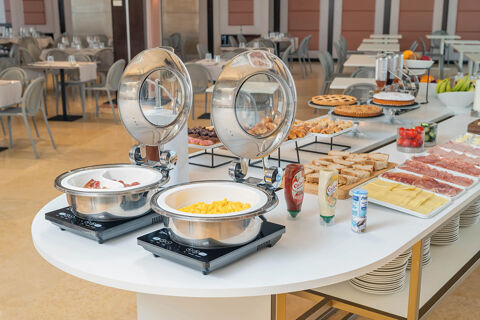 Breakfast buffet at B&B Hotel San Mauro featuring scrambled eggs, bread, cold cuts, cheese, pastries, fruit, and sauces on a white table
