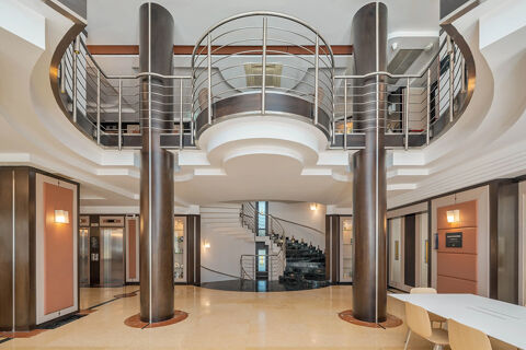 Lobby area with two large brown columns, a metal railing mezzanine, spiral staircase, elevator, and seating at B&B Hotel San Mauro