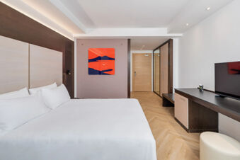 Modern hotel room at B&B Hotel San Mauro with large bed, wooden floor, wall art, TV, and built-in wardrobe with mirror