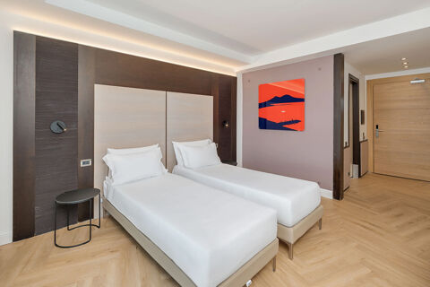 Two single beds with white linens and pillows in a modern room at B&B Hotel San Mauro with wood flooring and a painting on the wall