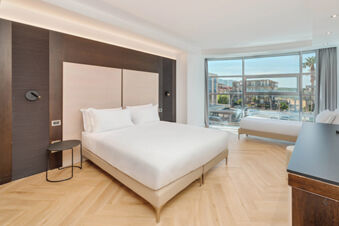 Spacious hotel room at B&B Hotel San Mauro with two beds, wood floors, large window, and city view outside