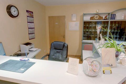 Reception desk of Hotel Garni Stadt Friedberg with a black office chair, glass jar with candies, and a clock on the wall