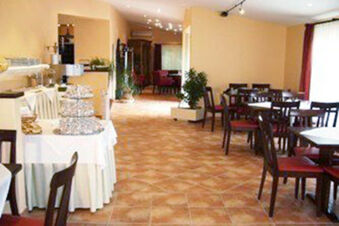 Dining area with multiple dark wooden tables and chairs, buffet table with food, and potted plants at Hotel Garni Stadt Friedberg