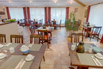 Dining area with wooden tables and chairs, set for breakfast with cups and bowls at Hotel Garni Stadt Friedberg