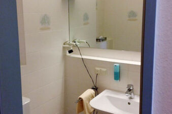 Small white tiled bathroom in Hotel Garni Stadt Friedberg with towel rack, sink, mounted hairdryer, mirror, and soap dispenser