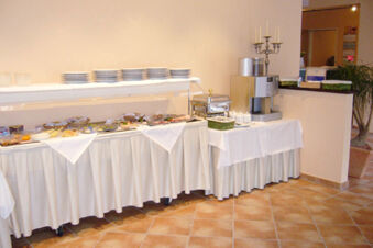 Buffet table at Hotel Garni Stadt Friedberg with plates, glass containers, food trays, a coffee machine, and a candelabra on tiled floor