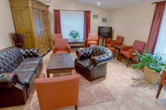 Hotel Garni Stadt Friedberg lounge with leather sofas, orange chairs, coffee tables, potted plants, and TV on wooden stand