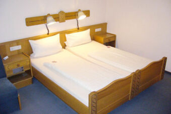 Two single beds with white bedding and wooden headboards between wooden nightstands in a Hotel Garni Stadt Friedberg room