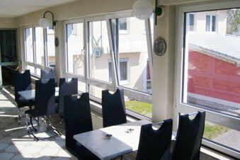Indoor seating area at Hotel Garni Stadt Friedberg with black chairs, white tables, large windows, and wall lamps visible