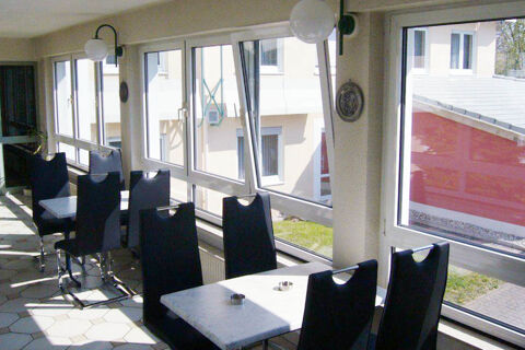 Indoor seating area at Hotel Garni Stadt Friedberg with black chairs, white tables, large windows, and wall lamps visible