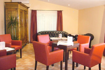A seating area with four red chairs around a square wooden table and a black leather sofa at Hotel Garni Stadt Friedberg