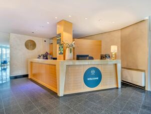Reception desk area with wooden paneling, a large round clock, a potted plant, a lamp, and signage at B&B Hotel Bergamo Executive