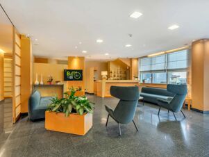 Modern lobby area of B&B Hotel Bergamo Executive with blue seating, potted plants, wooden reception desk, and large windows
