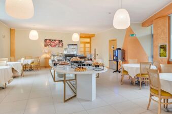 Breakfast buffet table with pastries, cakes, and coffee machine in a spacious dining area at B&B Hotel Bergamo Executive