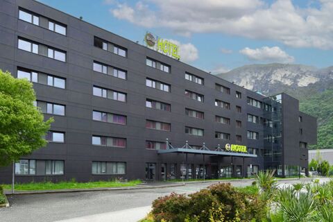 Large dark gray multi-story building with many windows, green trees, and B&B Hotel Trento signage on the roof and entrance area