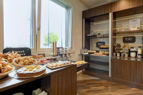 Breakfast buffet counter with assorted pastries, breads, cereals, and jars displayed in a well-lit room at B&B Hotel Trento