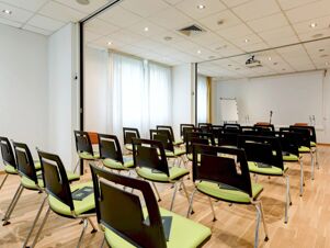 Conference room at B&B Hotel Trento with rows of black and green chairs, a whiteboard, and a projector on the ceiling