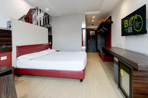 Hotel room at B&B Hotel Trento with a red bed frame, white bedding, wall-mounted TV, wooden desk, and open clothes hangers space