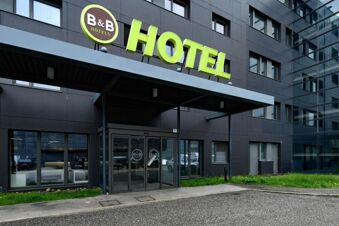 Exterior view of a modern dark building with a glass entrance and green B&B Hotel Trento sign above the door
