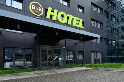 Exterior view of a modern dark building with a glass entrance and green B&B Hotel Trento sign above the door