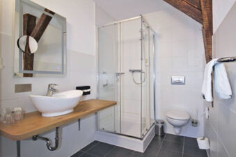 Bathroom interior of Hotel G&auml;stehaus Centro Albert GmbH featuring a wooden countertop with vessel sink, glass shower enclosure, and wall-mounted toilet