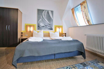 Double bed with white pillows, folded towels, gray bedspread, wooden wardrobe, and a window in Hotel G&auml;stehaus Centro Albert GmbH room