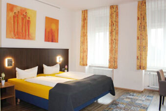 Double bed with yellow sheets, white pillows, dark headboard and bedside lamps in a bright room at Hotel G&auml;stehaus Centro Albert GmbH