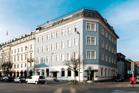 Large light blue and white corner building with multiple windows along a street housing Hotel G&auml;stehaus Centro Albert GmbH