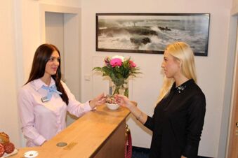 A receptionist in a pink shirt handing a key to a blonde woman across the wooden counter at Hotel G&auml;stehaus Centro Albert GmbH