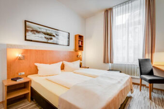 Bedroom in Hotel G&auml;stehaus Centro Albert GmbH with twin beds, white linens, wooden furniture, and a large window with curtains