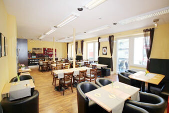 Dining area with wooden chairs and black armchairs, yellow walls, and large windows at Hotel G&auml;stehaus Centro Albert GmbH