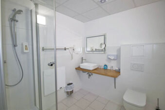 Modern white tiled bathroom with a glass shower cabin, floating sink counter, toilet, and amenities at Hotel G&auml;stehaus Centro Albert GmbH