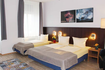 Hotel G&auml;stehaus Centro Albert GmbH room with two beds, bedside tables, wall lamps, window with curtains, and framed artworks