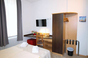 Hotel G&auml;stehaus Centro Albert GmbH room with twin beds, folded towels, wooden desk, chair, wardrobe, and wall-mounted TV