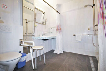 Accessible bathroom in Hotel G&auml;stehaus Centro Albert GmbH with toilet, shower curtain, grab bars, and a white stool with adjustable legs
