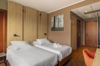 Two single beds with white linens and pillows against a wood-paneled wall in a room at B&B Hotel Cuneo Cristal