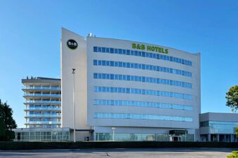 White multi-story building with horizontal windows and the green sign B&B Hotels on top visible against a clear blue sky at B&B Hotel Cuneo Cristal