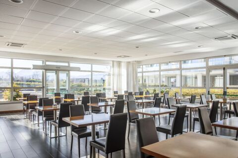 Dining area with multiple tables and black chairs, large windows letting in natural light at B&B Hotel Cuneo Cristal