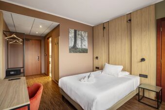 Bedroom at B&B Hotel Cuneo Cristal with a double bed, wooden closet panels, small glass side table, and brown walls with forest artwork