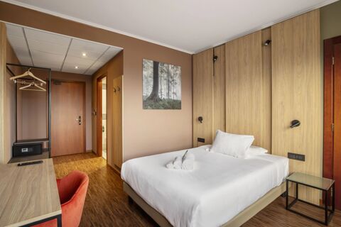 Bedroom at B&B Hotel Cuneo Cristal with a double bed, wooden closet panels, small glass side table, and brown walls with forest artwork