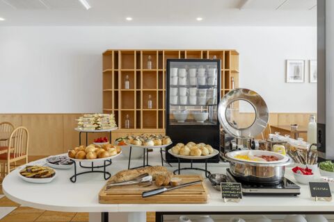 Breakfast buffet with various breads, packaged yogurts, scrambled eggs, and condiments in a dining room at B&B Hotel Cuneo Cristal